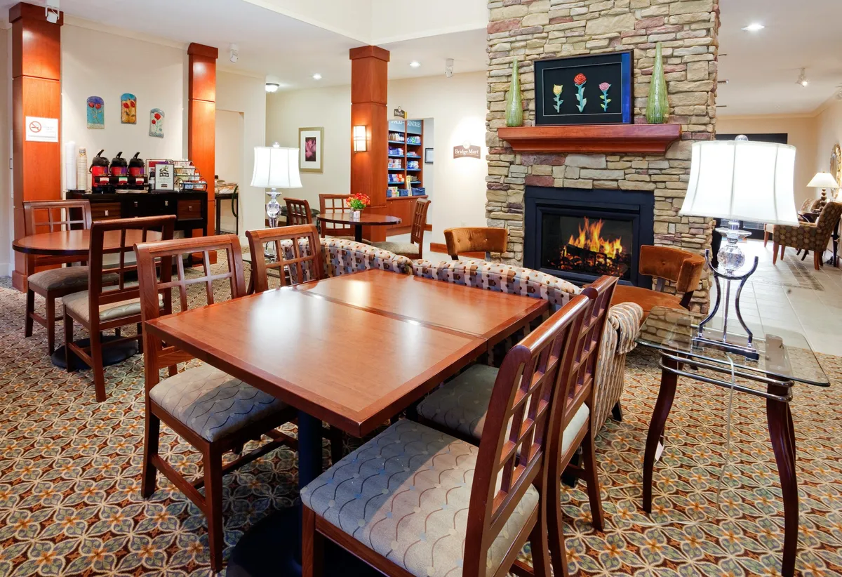 An inviting lounge area featuring a fireplace, wooden tables, armchairs, decorative art, and soft lighting. Guests are seen socializing, reading, and relaxing by the fire, creating a welcoming atmosphere perfect for informal networking or winding down after a busy day.